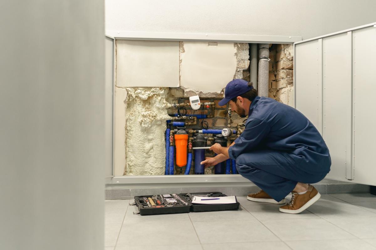Plumber crouched at a customer's utility closet, mid-repair